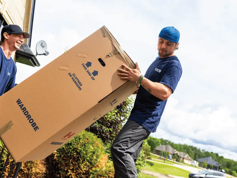 Two movers carrying large wardrobe box outside home