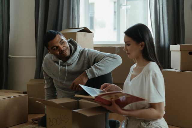 Couple unpacking boxes in new apartment, reading book