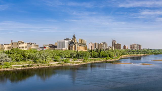 Downtown skyline along river with trees and blue sky