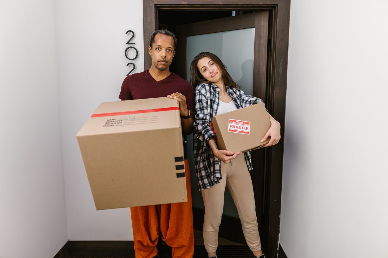 Tired couple holding cardboard moving boxes while standing outside apartment doorway