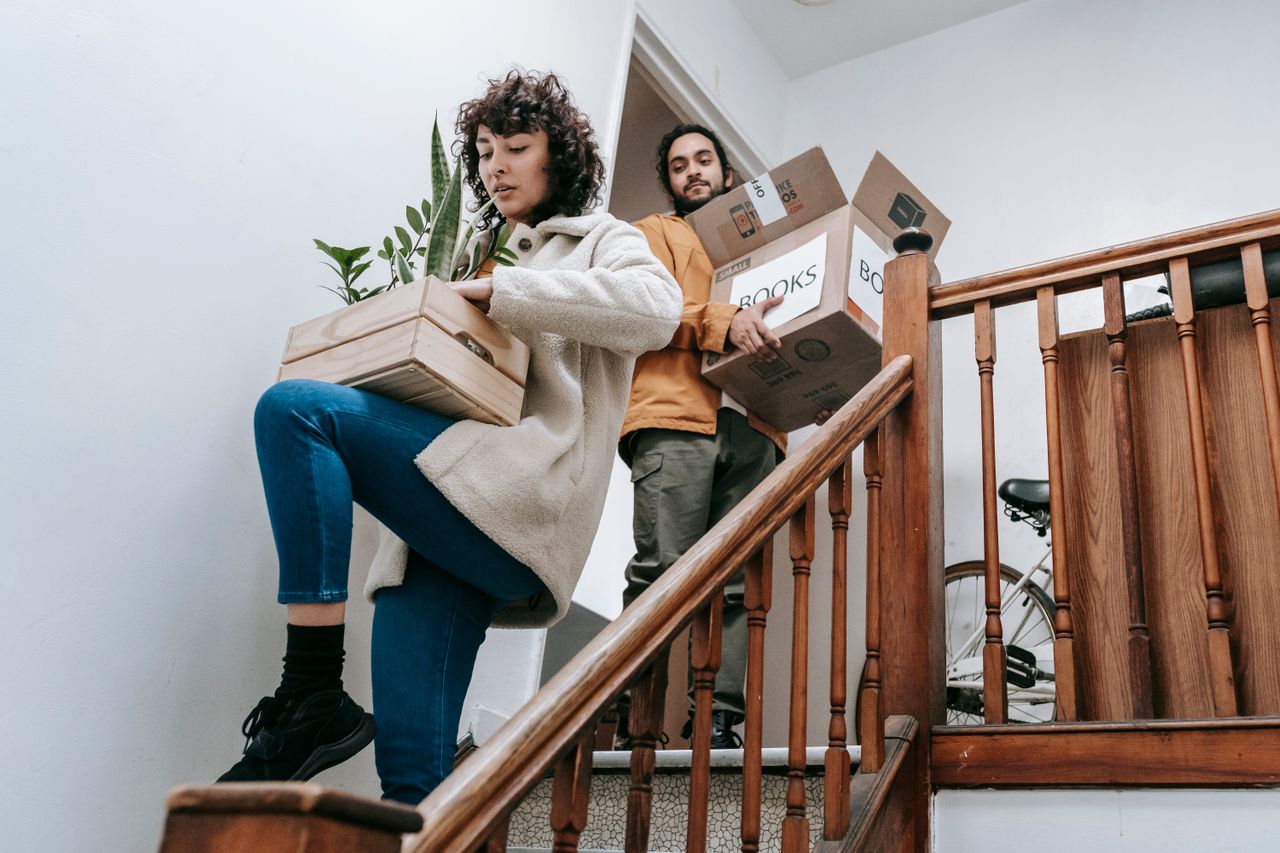 Man and woman carrying moving boxes down stairs during house relocation